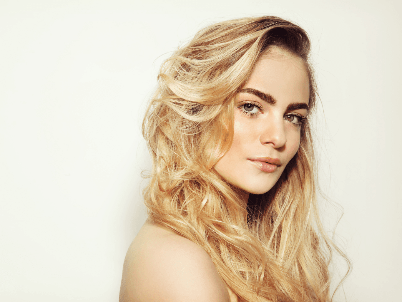 Young woman with soft blonde waves and natural-looking half head highlights, facing forward with a gentle smile.