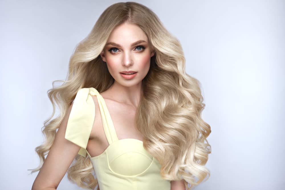 Woman with long, voluminous blonde hair extensions styled in soft waves, showcasing a premium salon look.