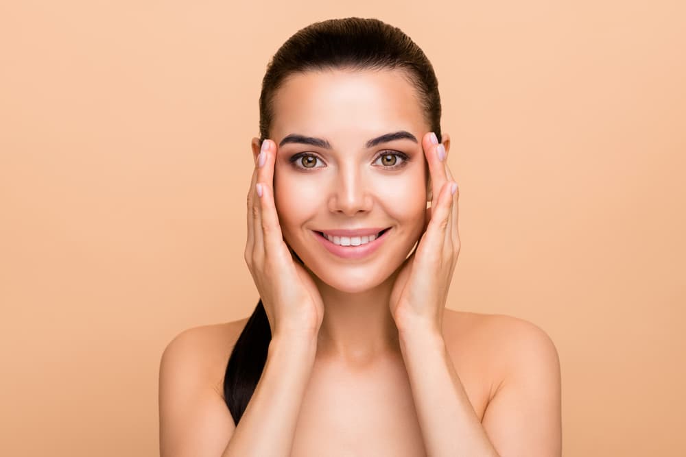 Woman with healthy, radiant skin smiling and touching her face after Polynucleotides Treatment in Biggleswade.