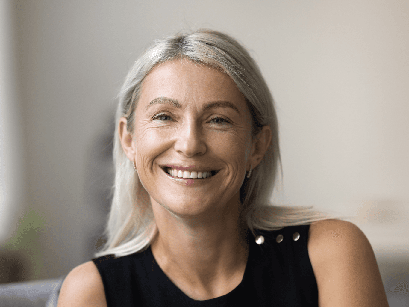 Smiling middle aged woman with natural grey blonde hair wearing a sleeveless black top, representing confidence and wellbeing during menopause.