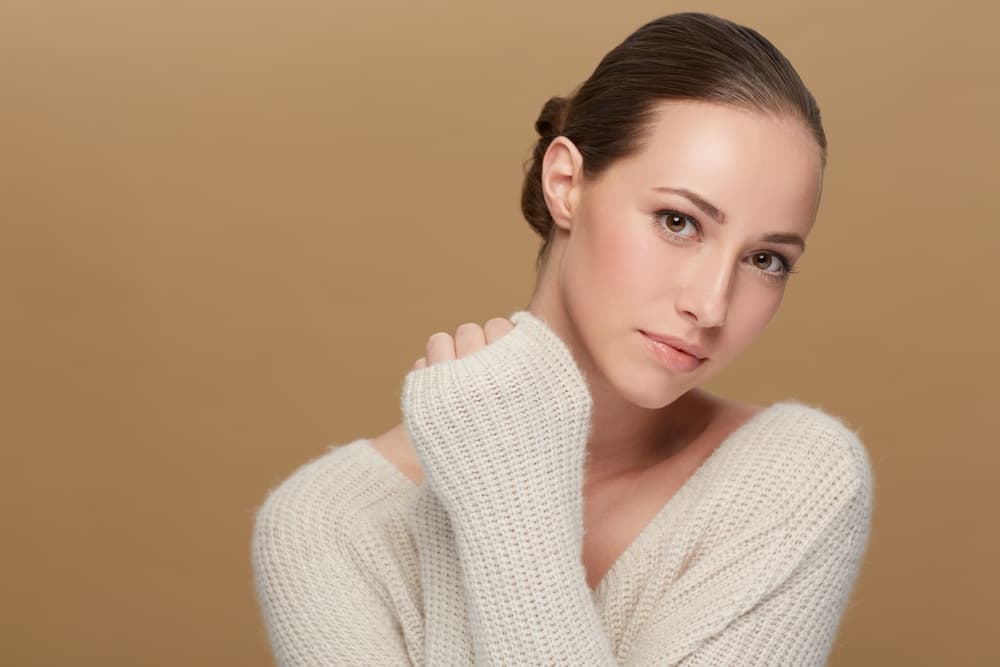 Woman with smooth skin wearing a cosy cream sweater, representing how skin needs extra care in winter.